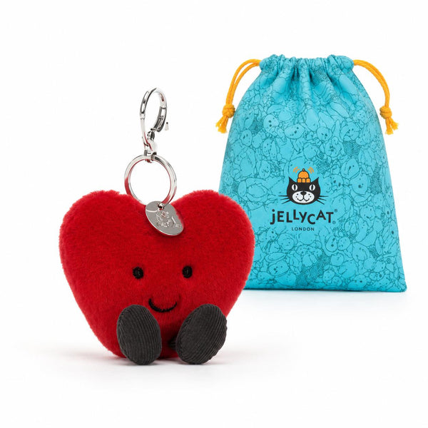 Red heart-shaped plush toy with a keychain and a blue drawstring bag featuring a logo on a white background.